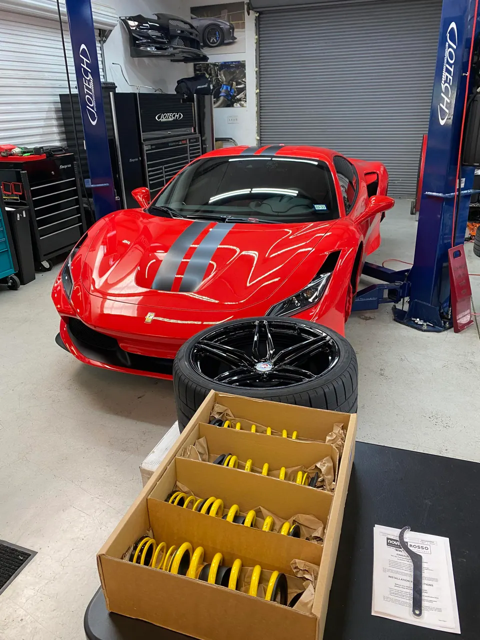 Red Ferrari F8 Tributo on a lift in a performance shop, with new suspension springs and a wheel ready for installation.