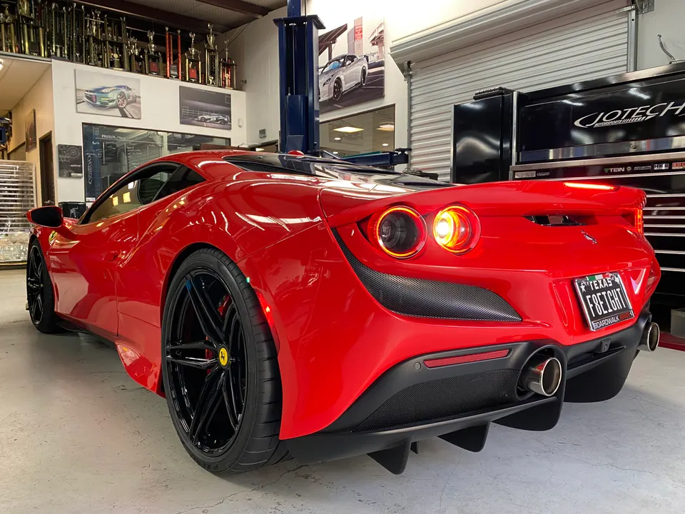 Red Ferrari F8 Tributo in a performance shop, showcasing its rear diffuser, exhaust tips, and black aftermarket wheels.