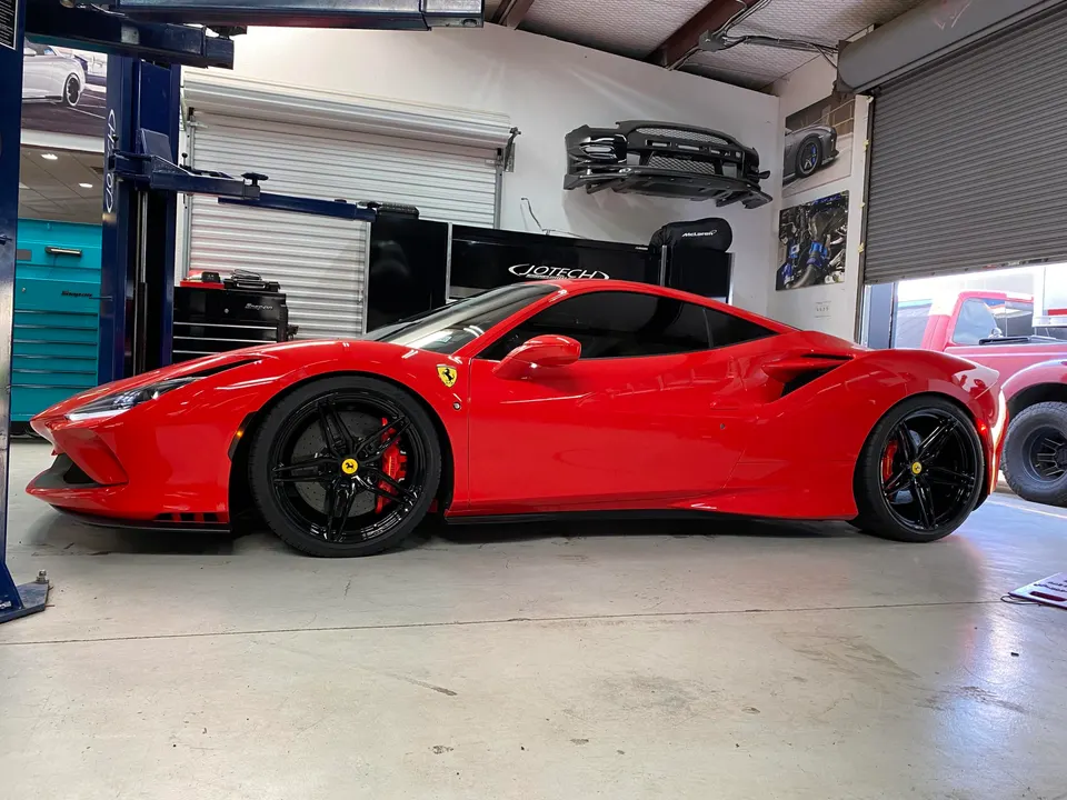 Red Ferrari supercar parked inside a performance tuning shop with a car lift and tools in the background.