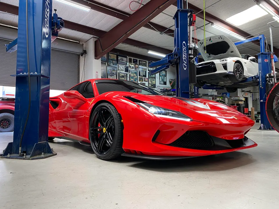 Red Ferrari F8 Tributo parked on a shop floor with a white Nissan GT-R elevated on a car lift in the background.