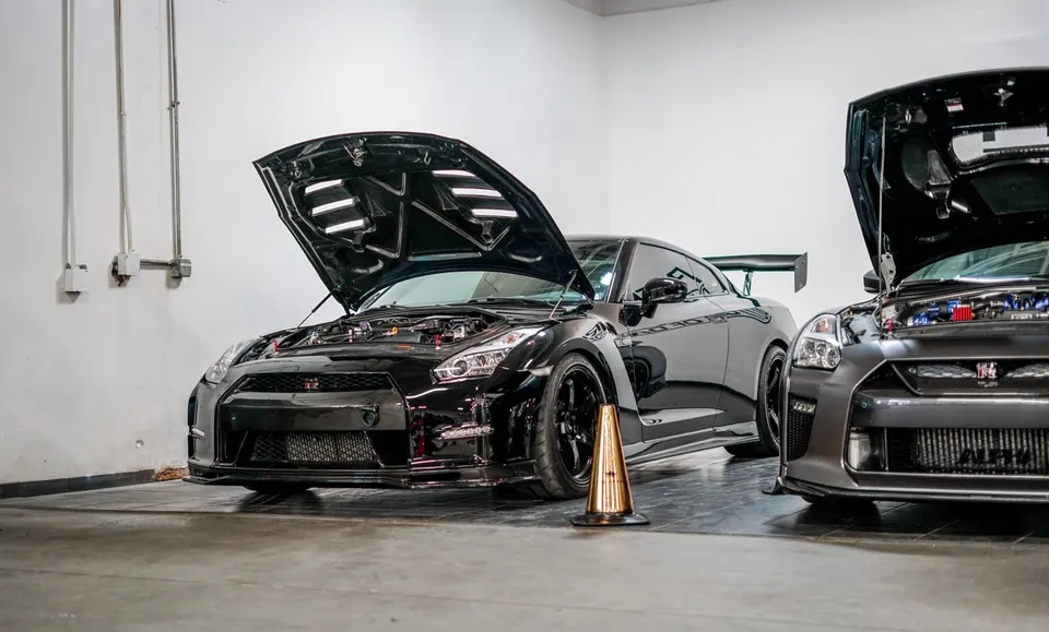 Two black Nissan GT-R R35s with open hoods showcasing their modified engine bays and performance parts in a shop.