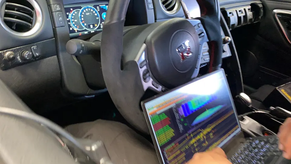 Interior view of a Nissan GT-R with a laptop displaying tuning software, showing a technician performing ECU calibration.