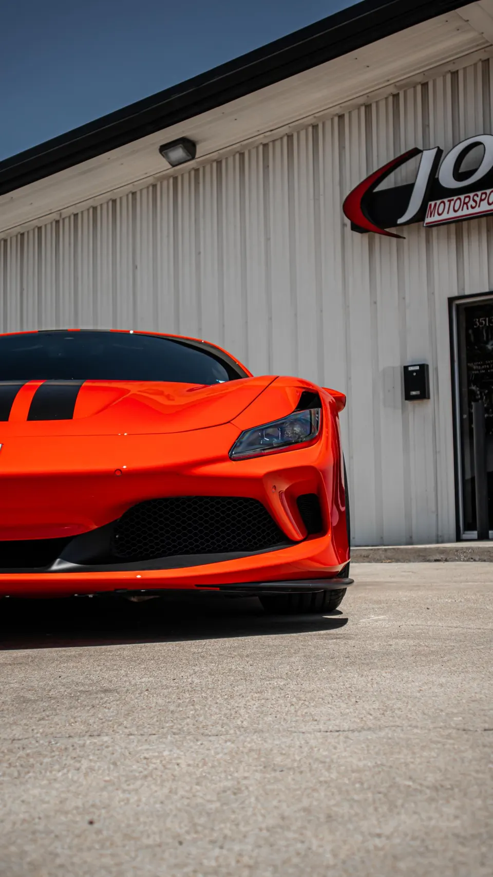 Orange Ferrari F8 Tributo sports car parked in front of the Jotech Motorsports building on a sunny day.