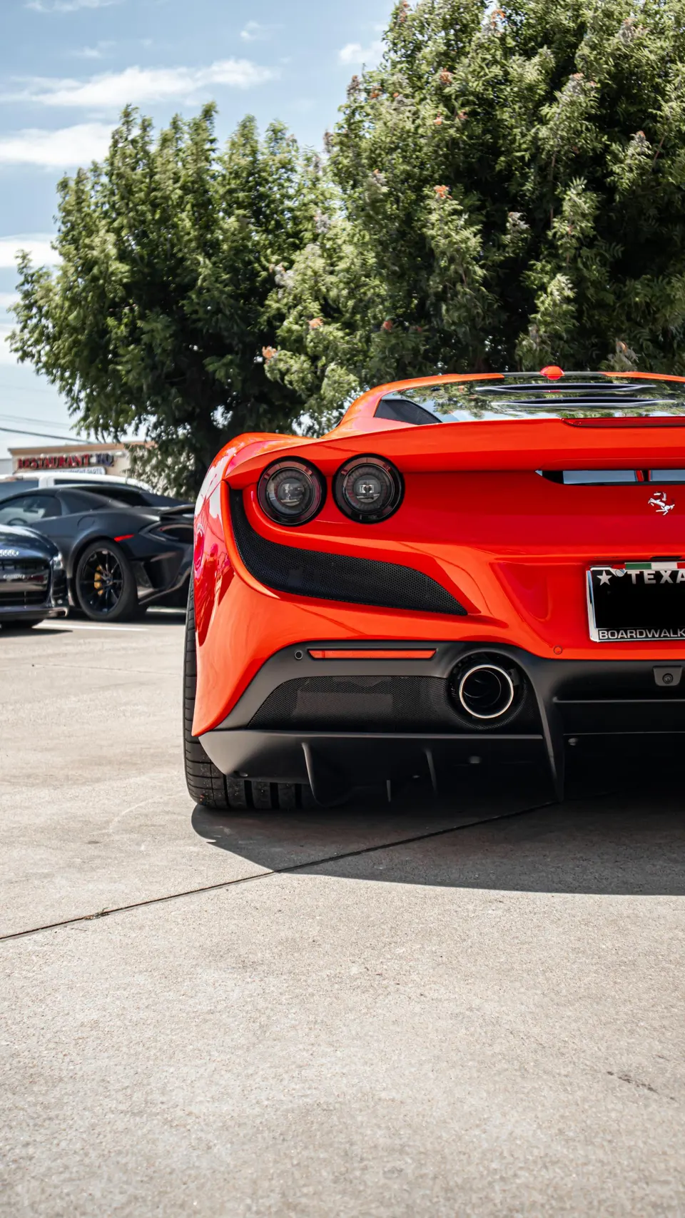 A vibrant red Ferrari F8 Tributo parked outdoors, showcasing its sleek rear design, exhaust tip, and aggressive diffuser.