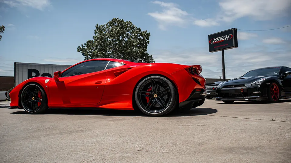 Red Ferrari 488 and black Nissan GT-R parked outside Jotech Motorsports shop on a sunny day.