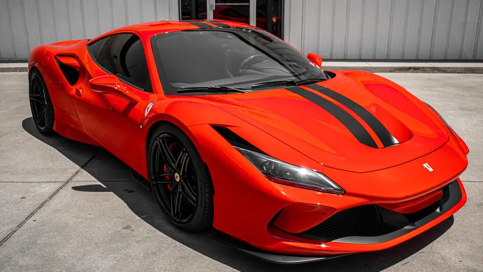 Red Ferrari F8 Tributo with black racing stripes parked outdoors, showcasing its sleek design and performance aesthetic.