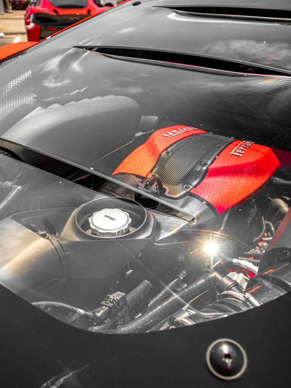 Close-up view of a Ferrari engine bay with a prominent red engine cover visible through the rear window.