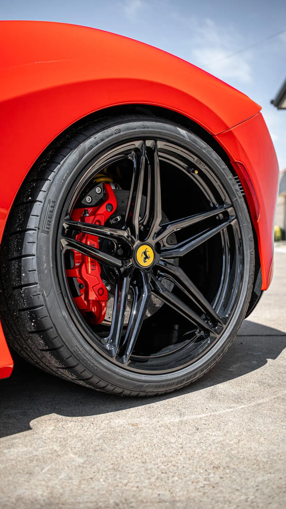 A close-up of a red Ferrari's black multi-spoke wheel with a yellow Ferrari logo and red brake calipers.