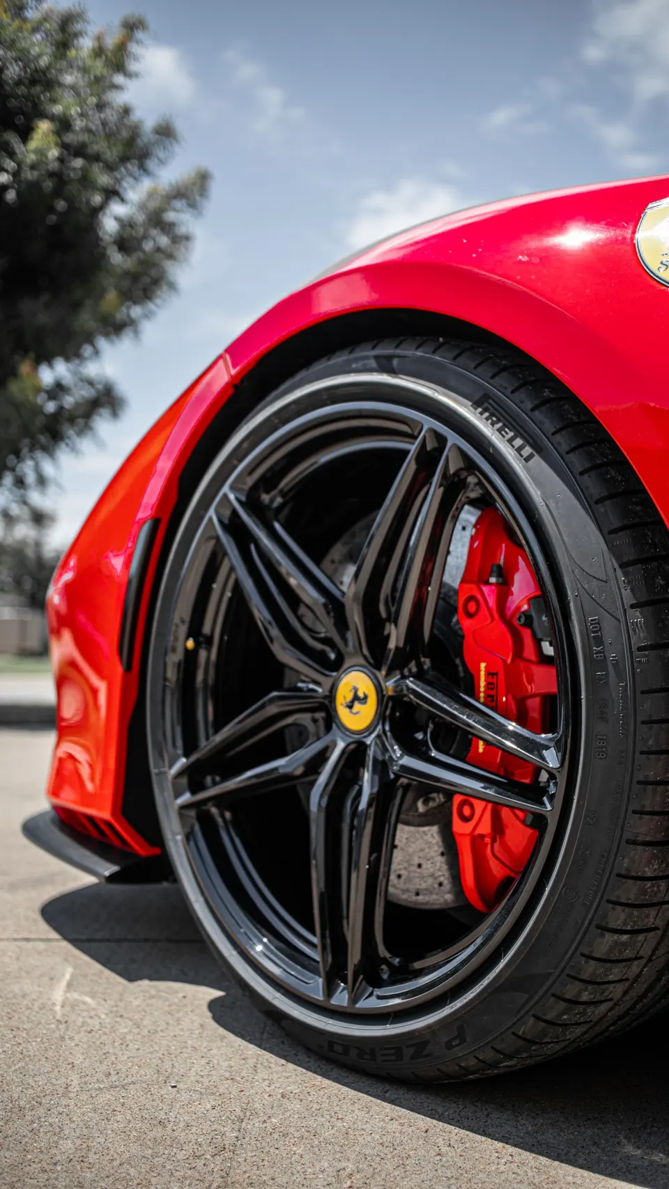 Close-up of a red Ferrari's black multi-spoke wheel with red brake calipers and Pirelli P Zero tire.