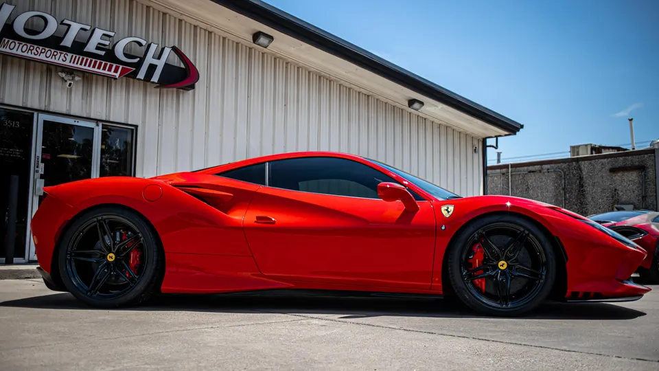A vibrant red Ferrari 488 supercar parked outside the Jotech Motorsports performance tuning shop on a sunny day.