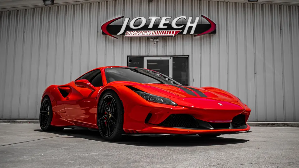 A red Ferrari F8 Tributo with black racing stripes parked in front of the Jotech Motorsports building.