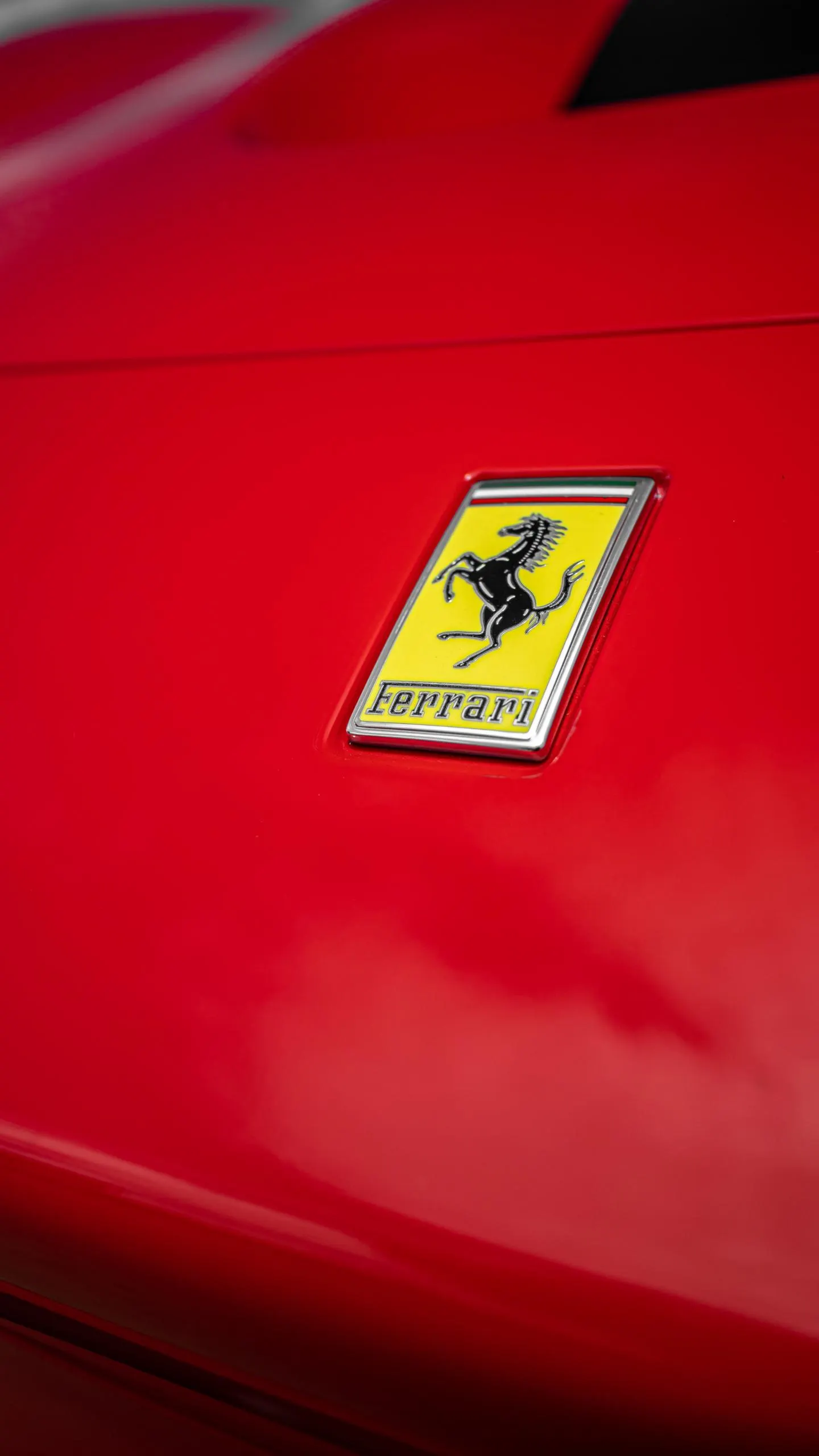 Close-up of a Ferrari emblem on the red paint of a luxury sports car.