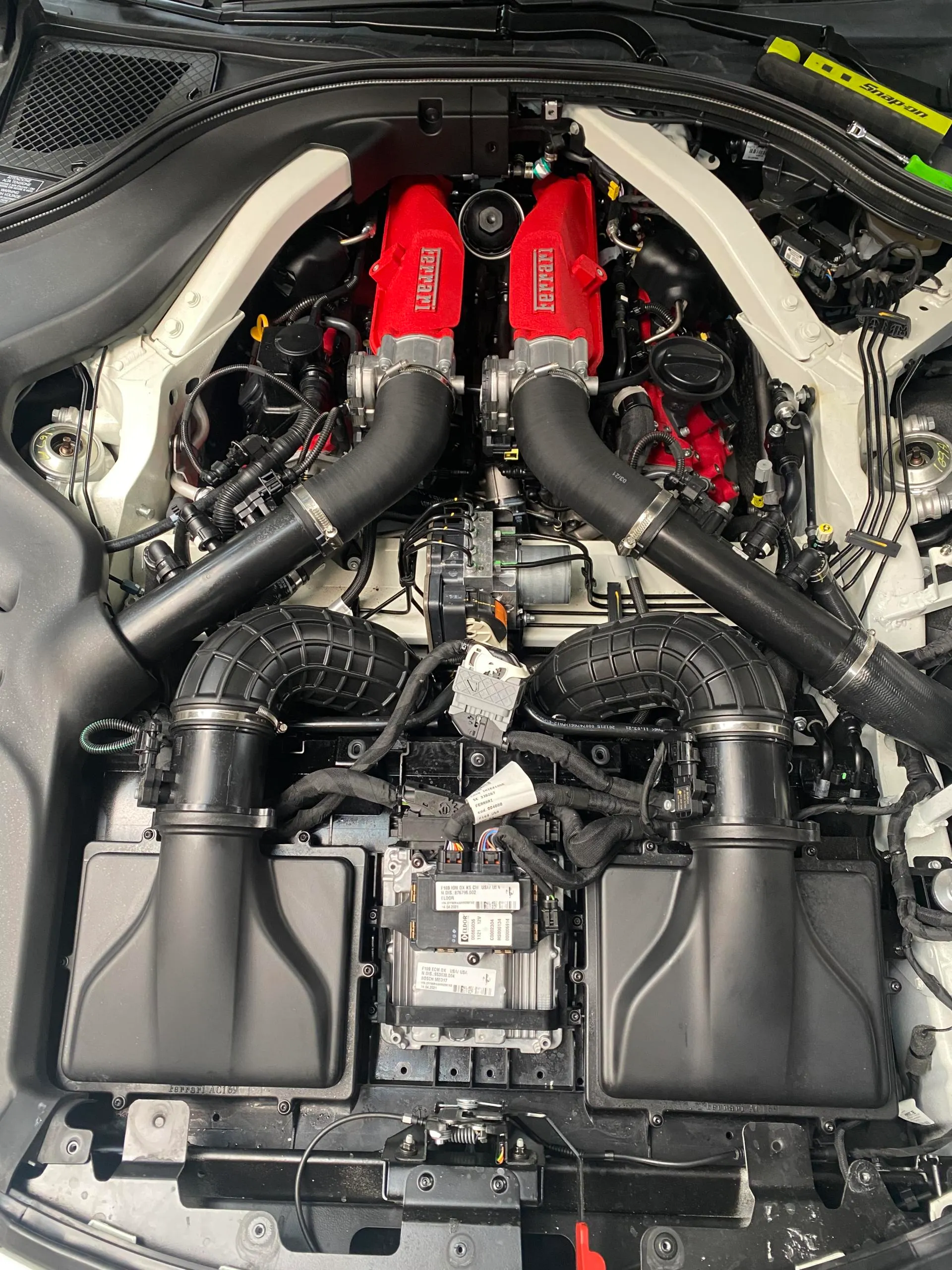 Detailed view of a Ferrari engine bay showcasing the V8 engine with red valve covers and black induction system components.