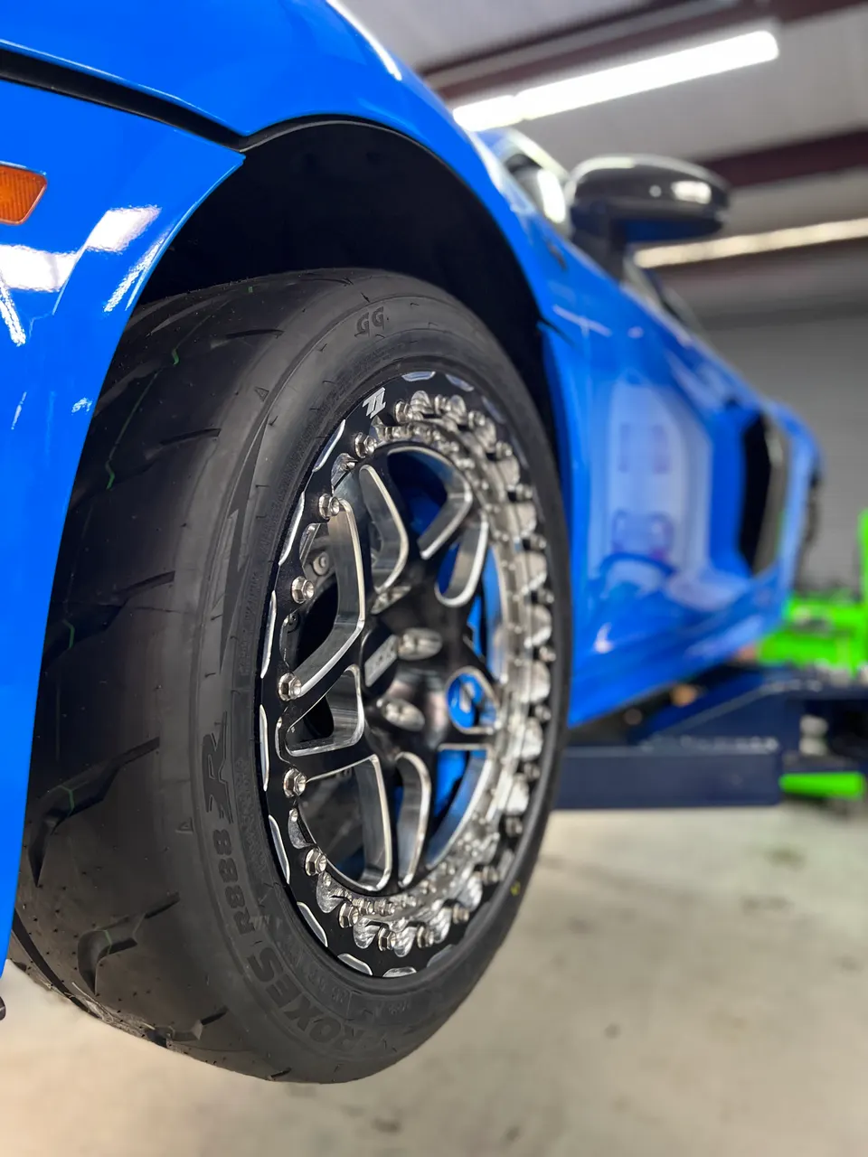 A blue car on a lift showcasing aftermarket drag wheels and Toyo R888R performance tires in a shop.