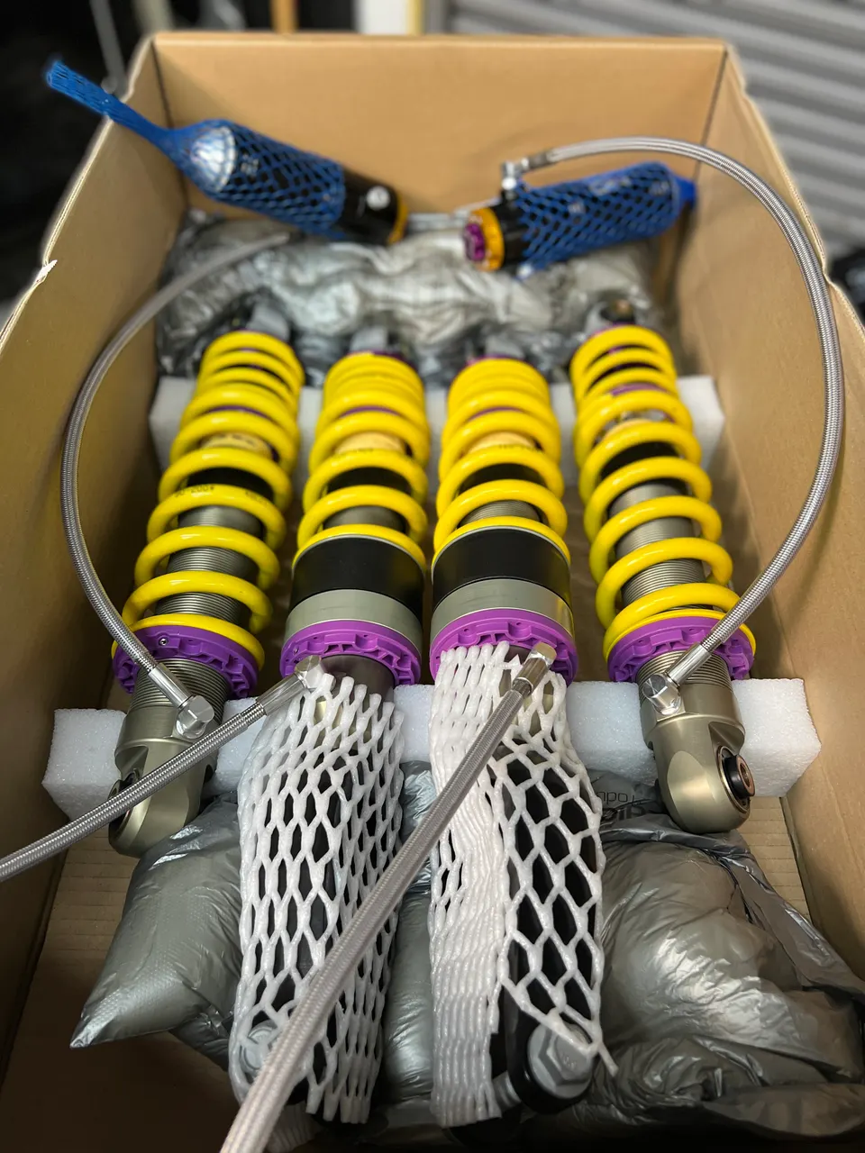 New KW coilovers for a performance car build, still in their packaging inside a cardboard box.