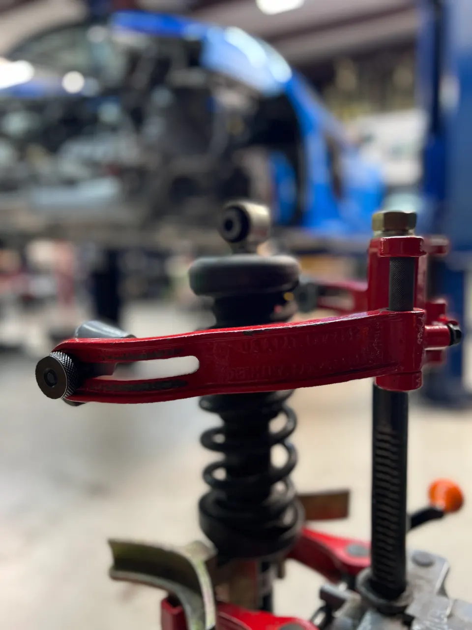 Close-up of a spring compressor tool working on a car's suspension coilover in a performance shop.