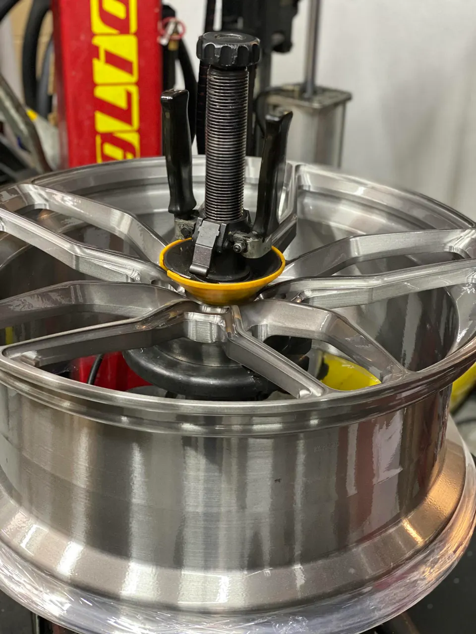 A silver multi-spoke wheel mounted on a tire changing machine in a workshop.