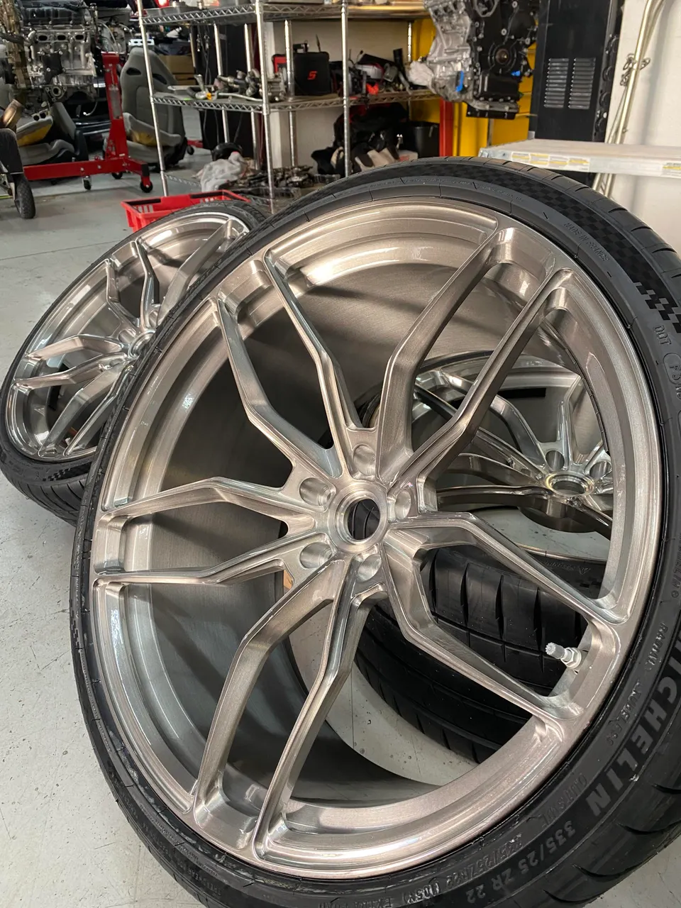 Close-up of custom forged multi-spoke wheels with Michelin performance tires in an automotive shop setting.