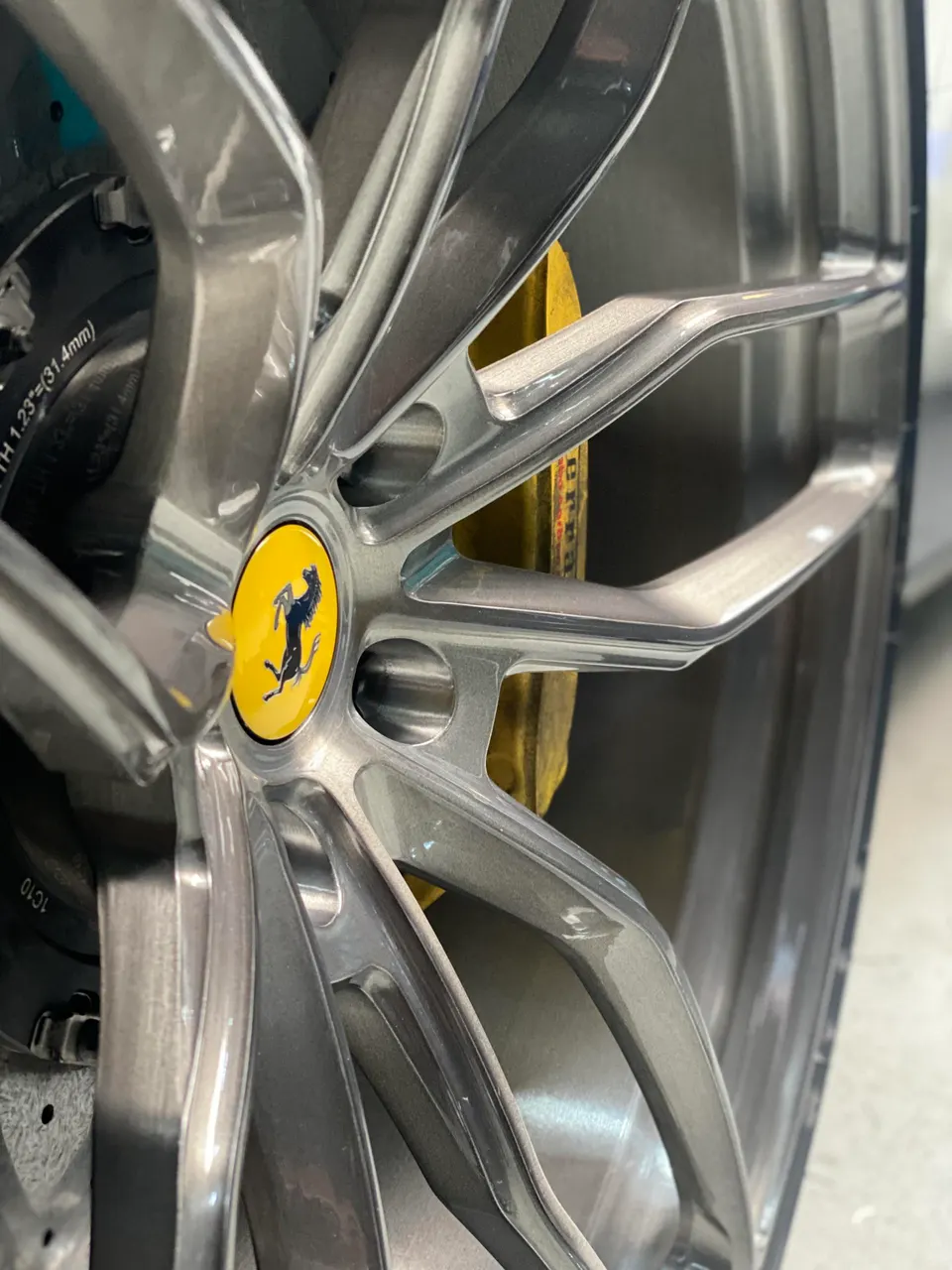Close-up of a Ferrari wheel with a yellow brake caliper and a Ferrari emblem on the center cap.