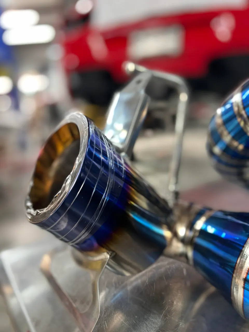 Close-up of a heat-treated titanium exhaust tip with blue and gold hues, showcasing intricate details.