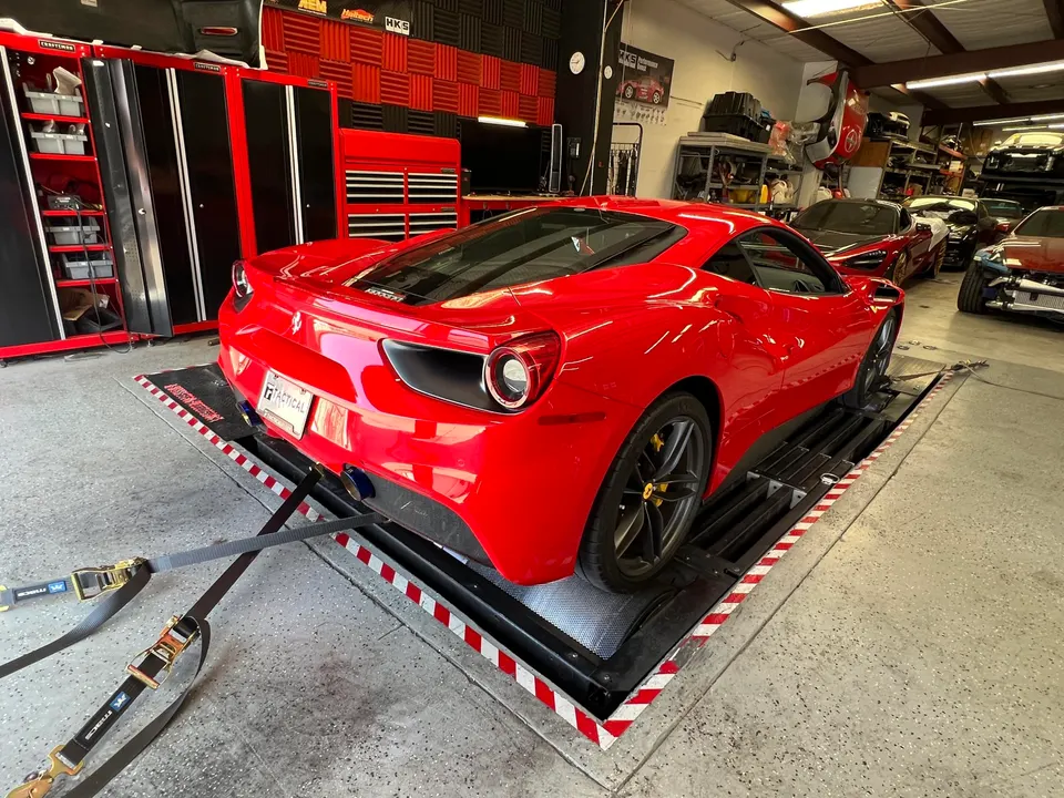 Red Ferrari 488 strapped to a dynamometer for performance tuning at a high-performance shop.
