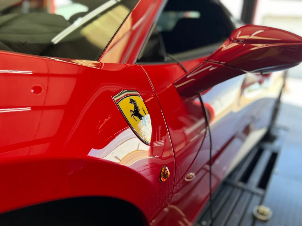 A close-up of a shiny red Ferrari fender with the iconic prancing horse emblem and side mirror.