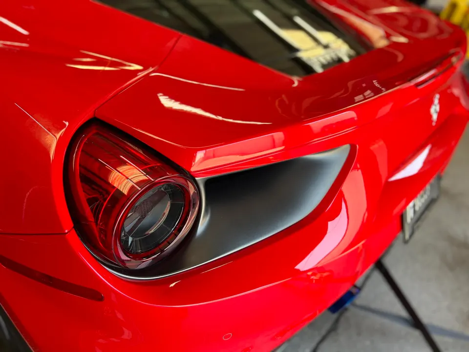 A close-up of the sleek red rear of a Ferrari sports car, highlighting the taillight and body lines.