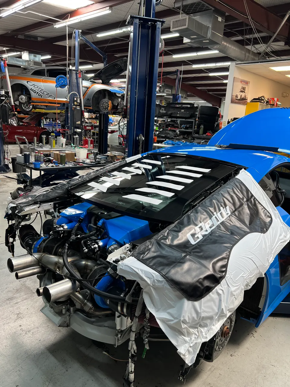 A blue Lamborghini Huracan with its front removed, revealing a twin-turbo engine build in a Jotech Motorsports shop.
