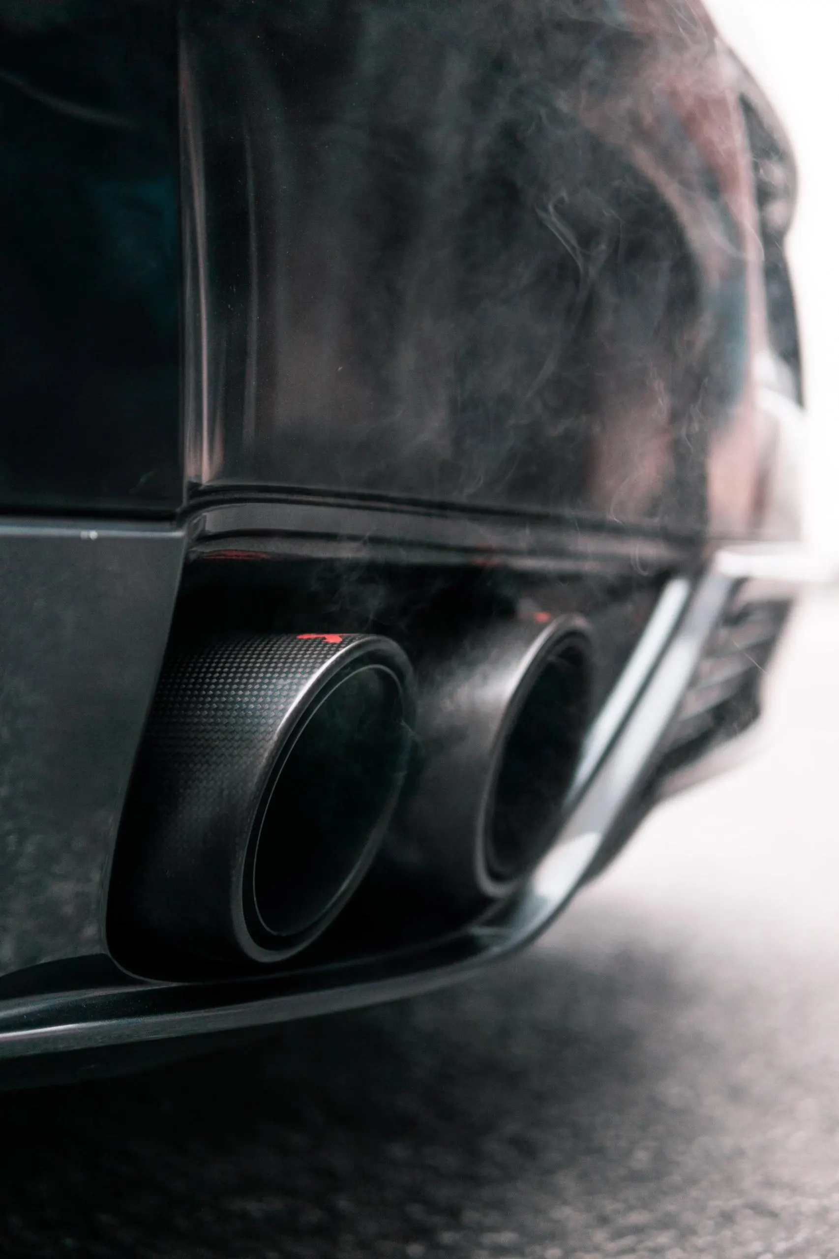 Close-up of a performance car's carbon fiber exhaust tips with smoke, showcasing the rear diffuser.