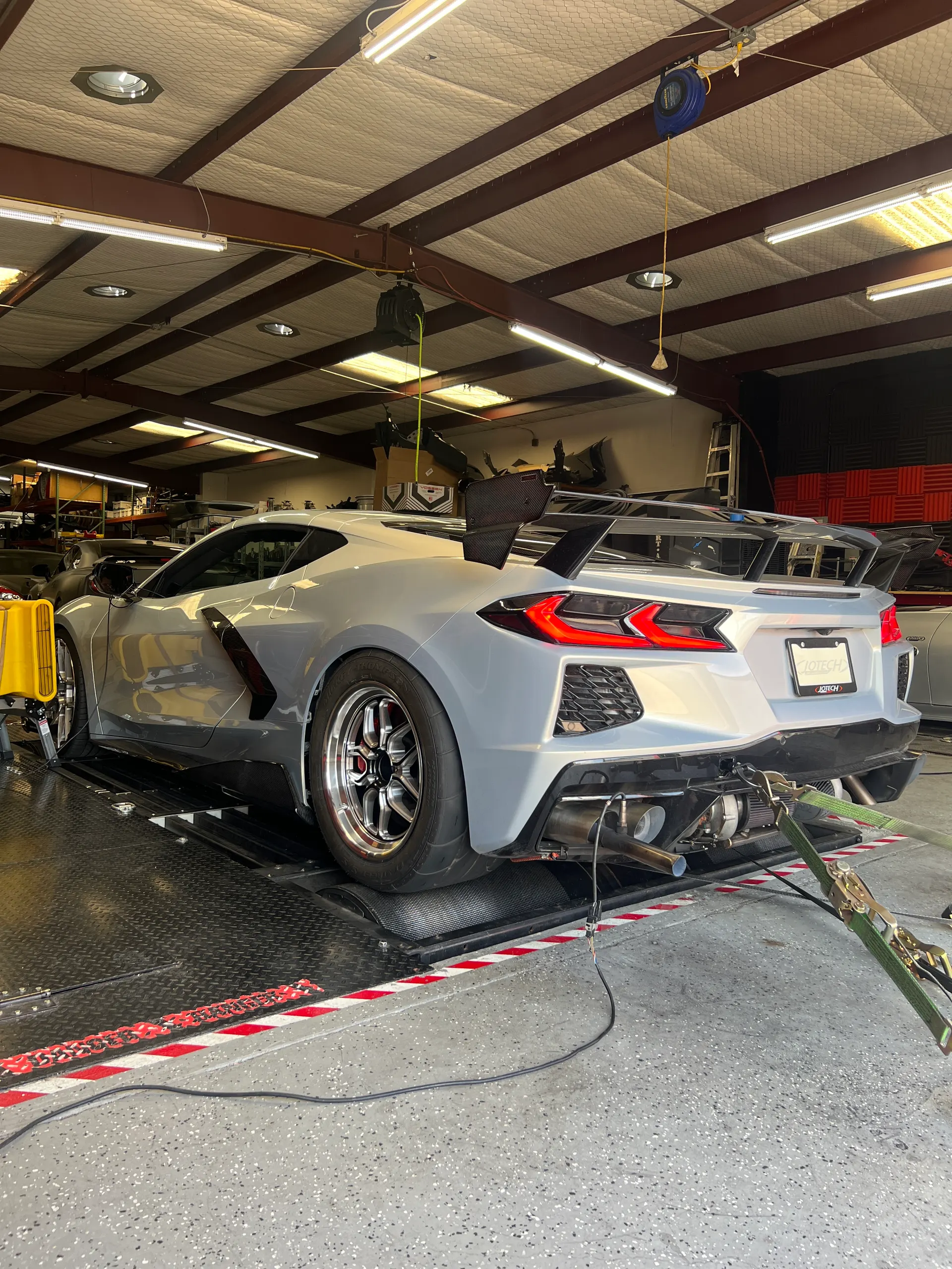 Gray C8 Corvette on a dynamometer undergoing performance testing with a custom exhaust system at Jotech Motorsports.