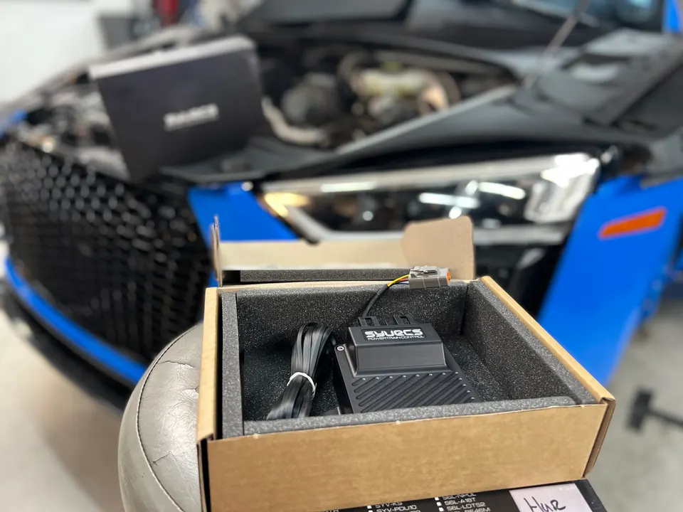 SYVURCS powertrain control module in a box, ready for installation on a blue Audi in a performance shop.