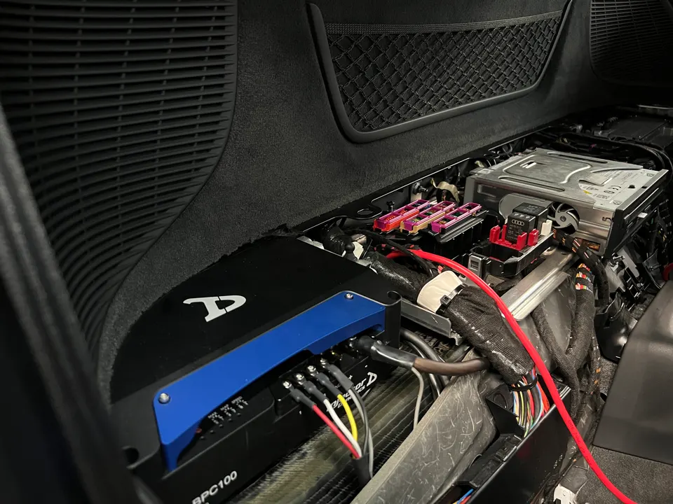 Custom car audio amplifier and wiring installation in a vehicle's rear compartment, showing fuses and cables.
