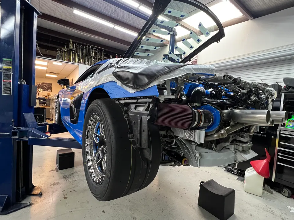 A blue C8 Corvette on a lift in a shop, with its rear bodywork removed to reveal a large turbocharger and custom exhaust.