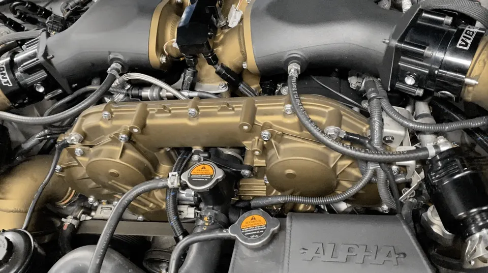 Close-up of a high-performance engine bay featuring a gold intake manifold, turbo boost piping, and Vibrant blow-off valves.
