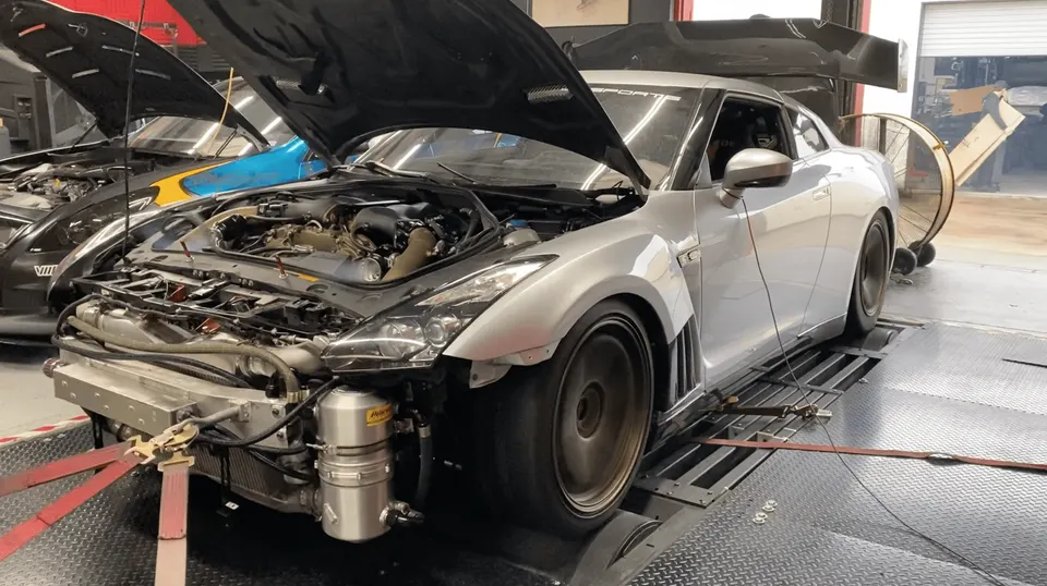 A silver Nissan GT-R R35 with its hood open, strapped to a dyno for performance testing at Jotech Motorsports.