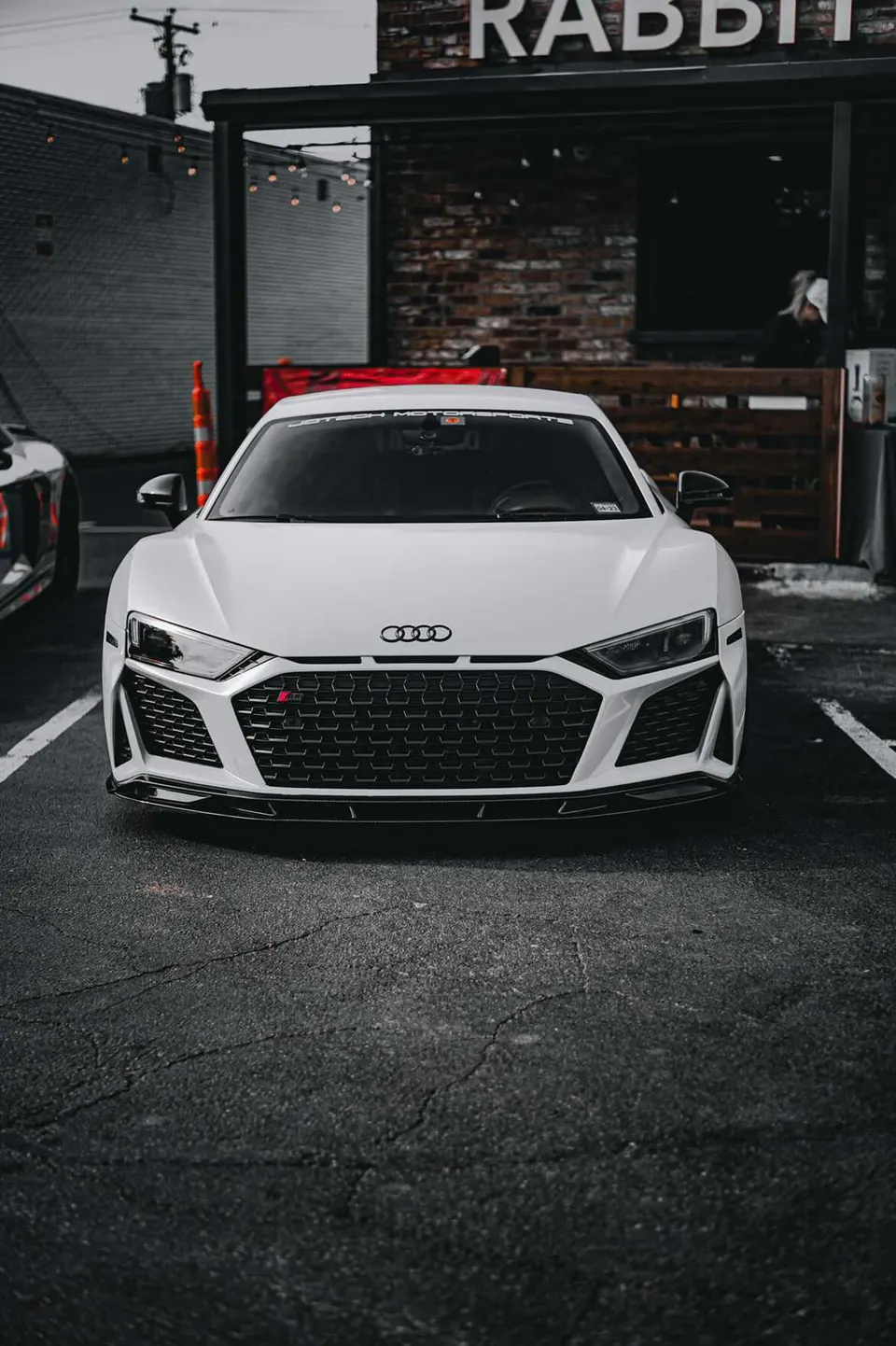 White Audi R8 supercar parked outdoors, featuring an aftermarket front splitter and Jotech Motorsports banner on the windshield.