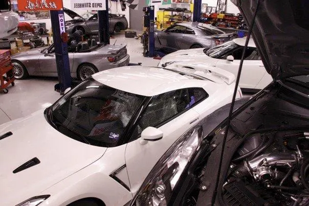 Multiple high-performance cars, including a white Nissan GT-R and a silver Honda S2000, in a Jotech Motorsports tuning shop.