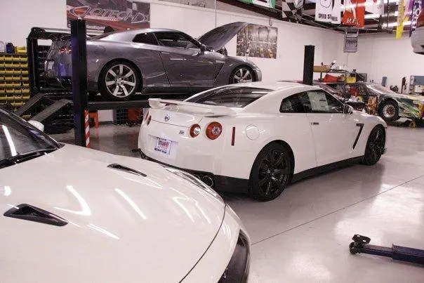 Multiple Nissan GT-R sports cars in a performance tuning shop, with one on a car lift and others on the floor.