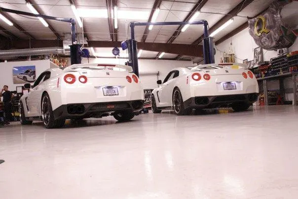 Two white Nissan GT-Rs parked in a Jotech Motorsports performance tuning shop with car lifts.