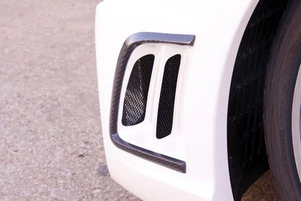 Close-up of a white car's fender vent with carbon fiber trim, showcasing exterior aero detail.