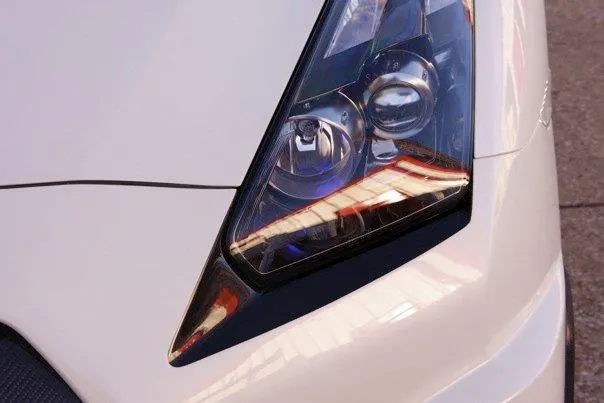 Close-up detail of a white car's front headlight and fender.
