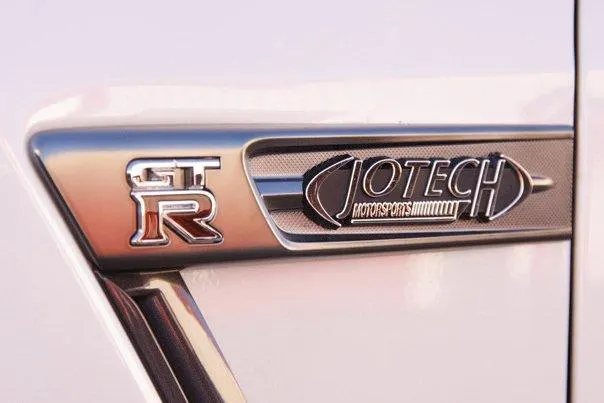 Close-up of a white Nissan GT-R fender with a chrome GT-R badge and a Jotech Motorsports badge.