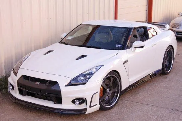 White Nissan GT-R R35 with aftermarket wheels and body kit parked outdoors in front of a building.