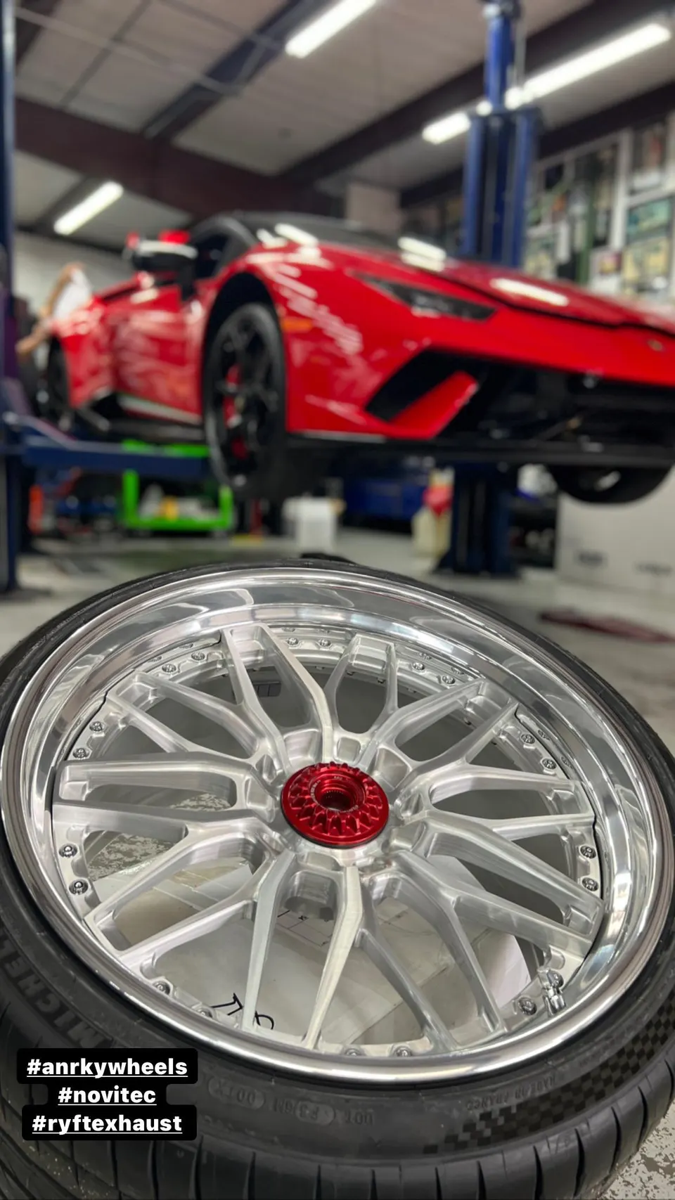 A red Lamborghini Huracan on a lift in a shop with a custom ANRKY wheel and tire in the foreground.