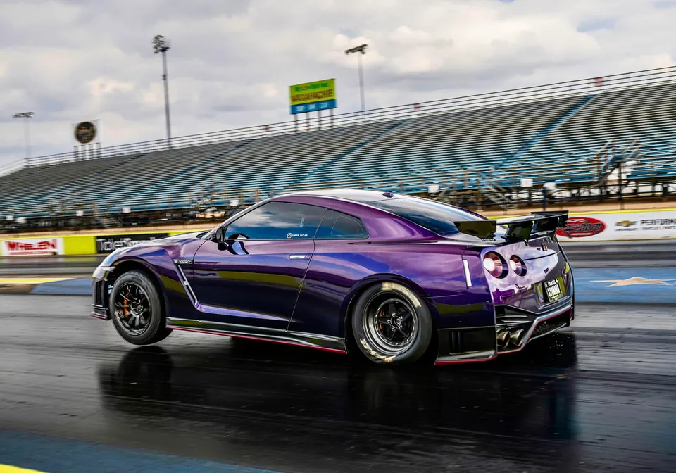 Purple Nissan GT-R on a drag strip with aftermarket wheels and a large rear wing, ready for a race.