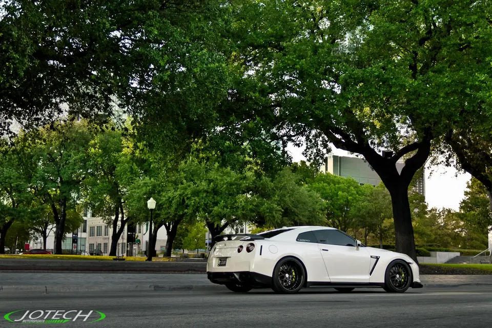 White Nissan GT-R with custom wheels and a carbon fiber rear wing parked on a city street, showcasing its sleek design.
