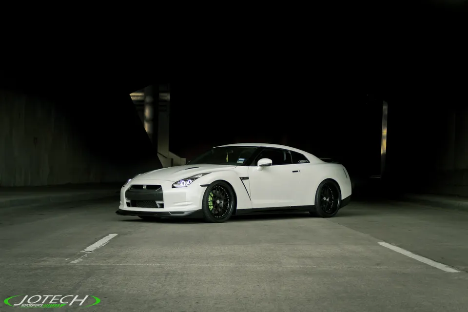 White Nissan GT-R R35 sports car with black wheels and green brake calipers parked in a dark underground setting.
