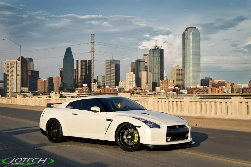 White Nissan GT-R parked on a bridge with the Dallas city skyline in the background, showcasing its sleek design.