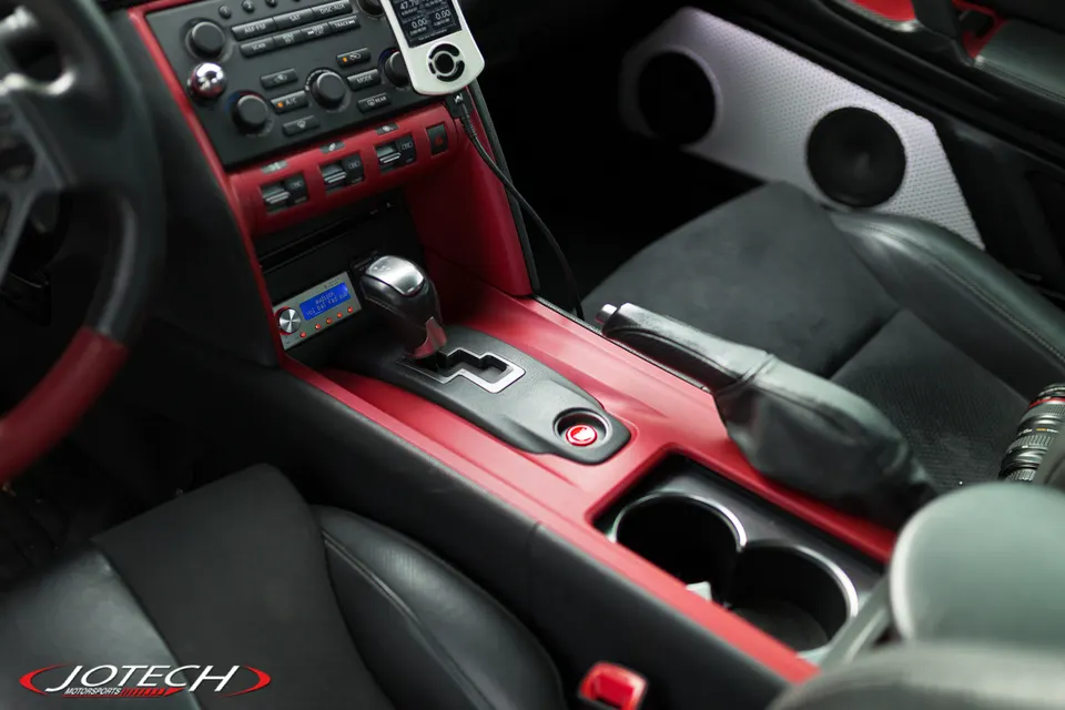 Detailed view of a Nissan GT-R interior with red trim, aftermarket head unit, and a Cobb Accessport on the dashboard.
