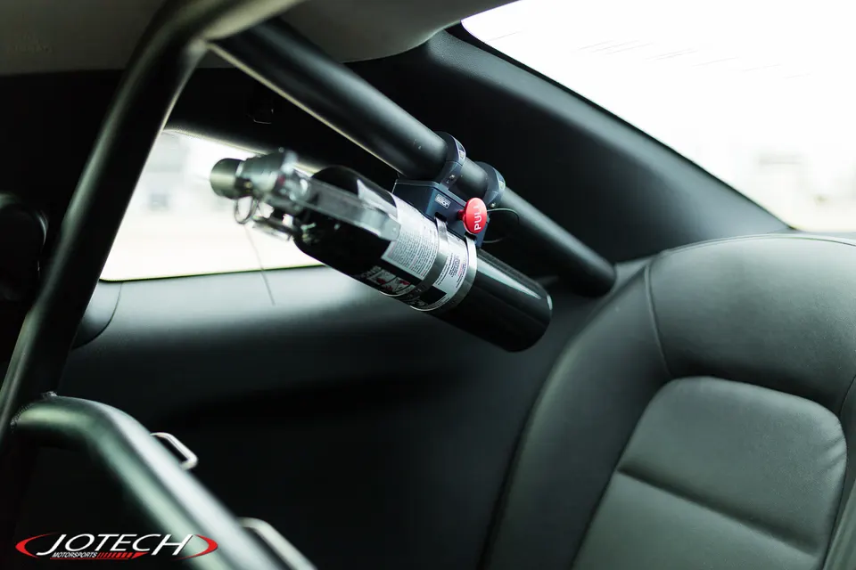Fire extinguisher mounted on a roll bar inside a performance car's interior, showcasing safety equipment.